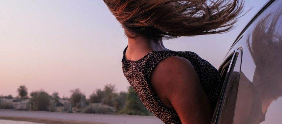 Woman with windblown hair leaning out car window, enjoying desert landscape