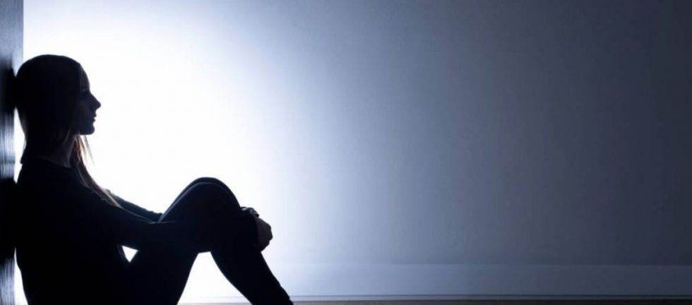 Silhouette of a young woman sitting alone, appearing sad or depressed.