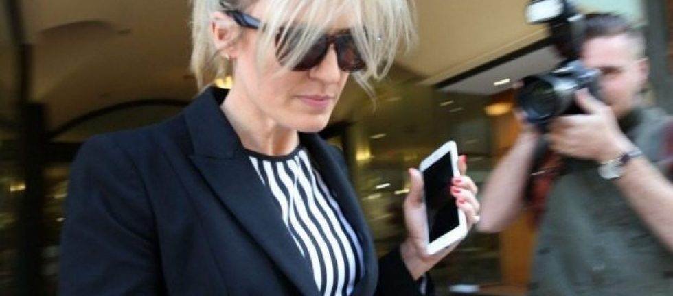 Woman in sunglasses leaving court, holding a smartphone.