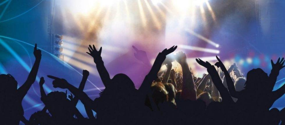 Silhouetted crowd at a music festival, hands raised in the air.