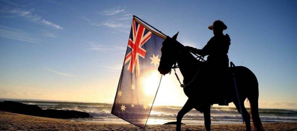 Silhouette of a soldier on horseback at sunset, holding an Australian flag.