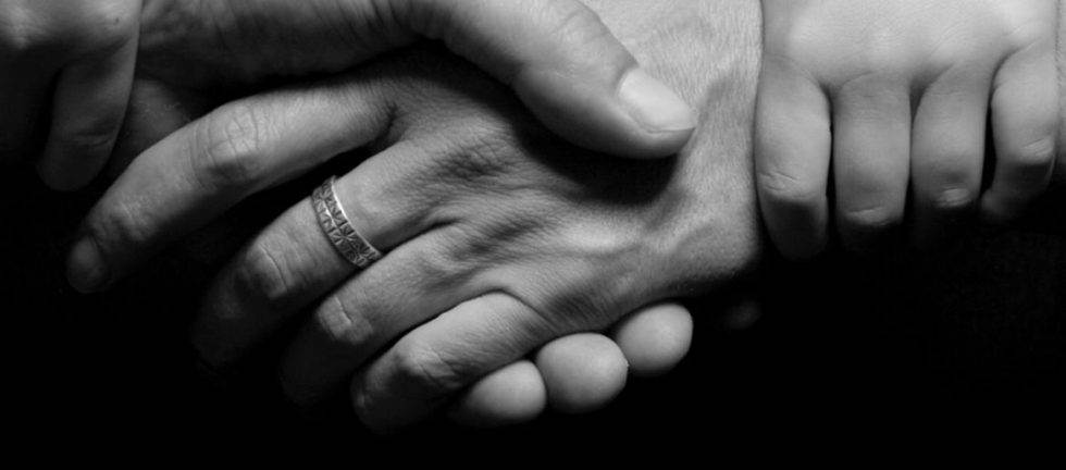 Close-up of three hands clasped together, showing connection and support.