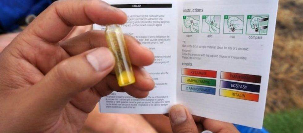 Person using drug testing kit, instructions visible, showing color chart for various substances.