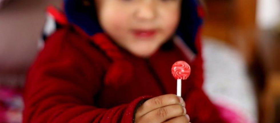 Child in red jacket holding a red and white swirl lollipop