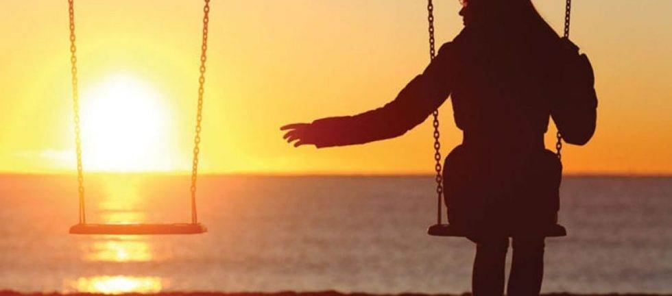 Silhouette of a woman sitting on a swing at sunset, reaching out towards the ocean.