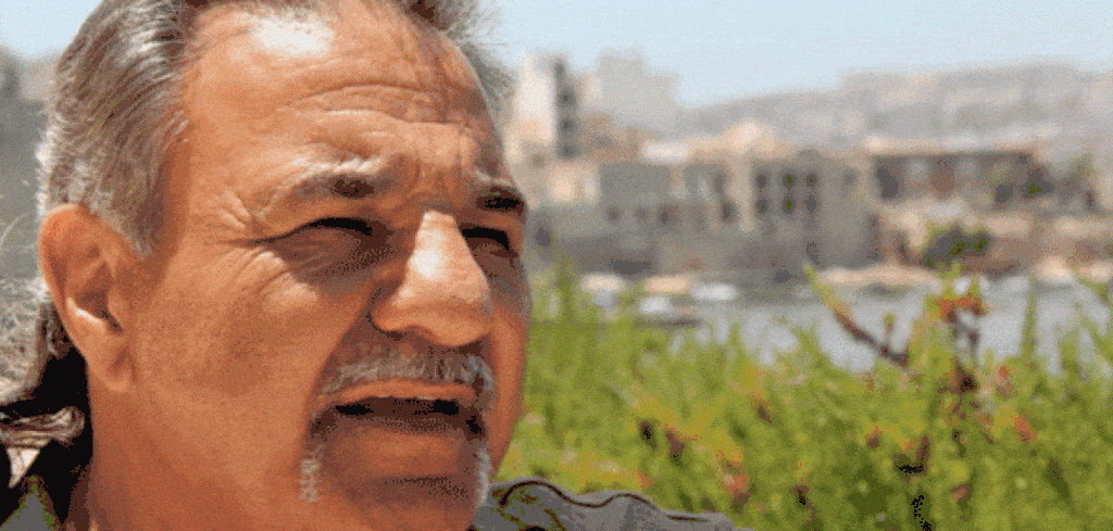 Close-up of an older man with graying hair and a mustache, speaking outdoors.