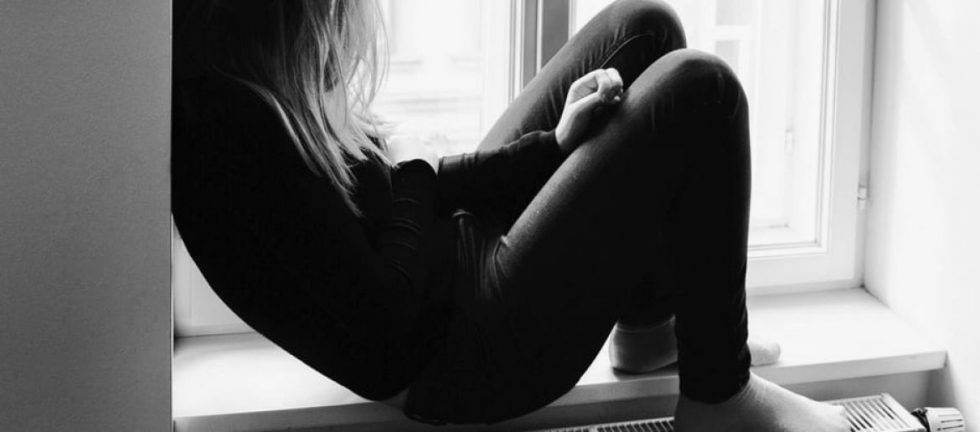 Young woman sitting by window, looking pensive.
