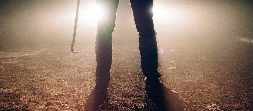 Person holding a crowbar, standing on dirt. Justice NSW