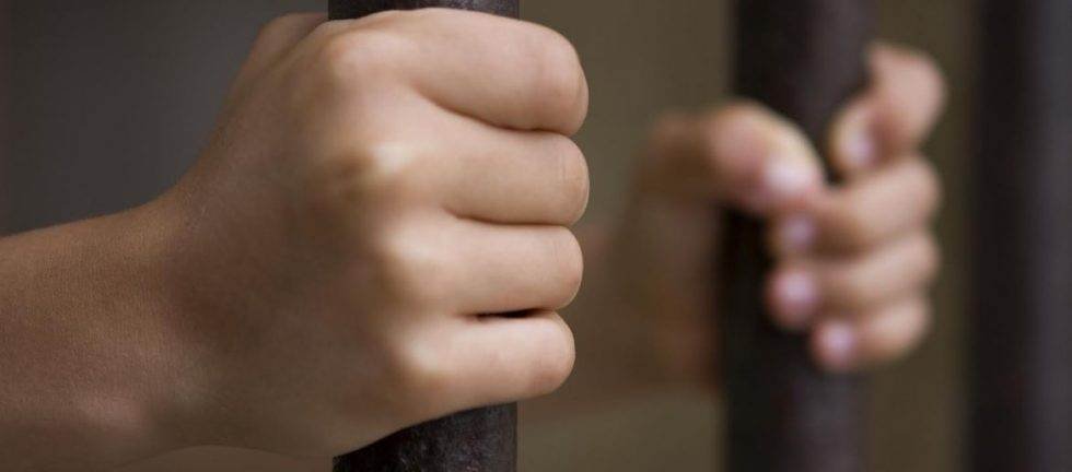 Close-up of hands gripping prison bars.