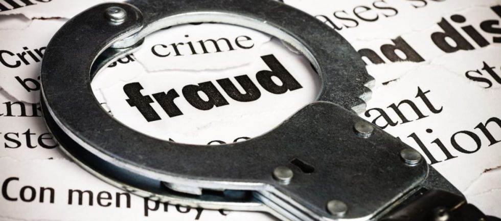 Handcuffs on newspaper with "fraud" headline; crime investigation concept.