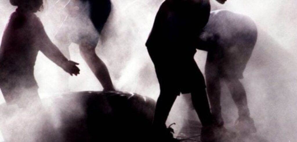 Silhouetted children playing in a misty spray of water.