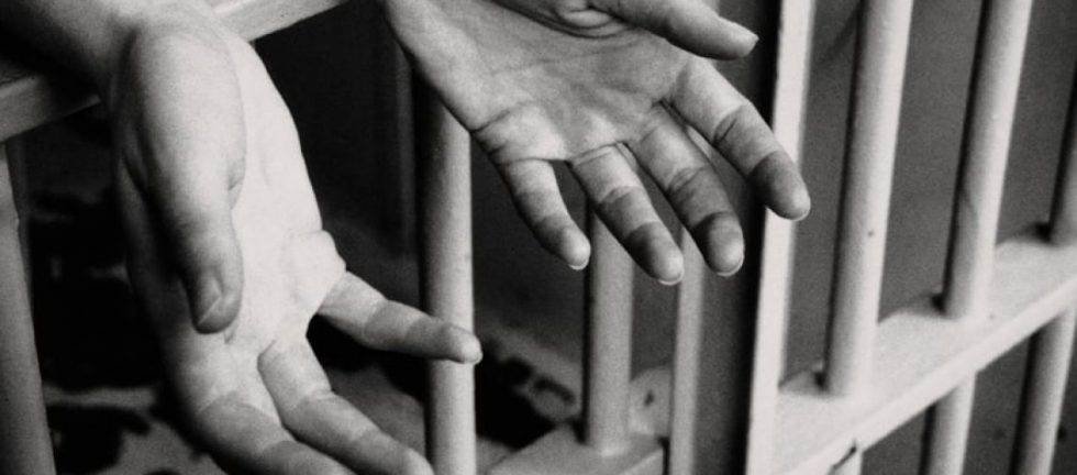Close-up of hands gripping prison bars. Imprisonment and incarceration.