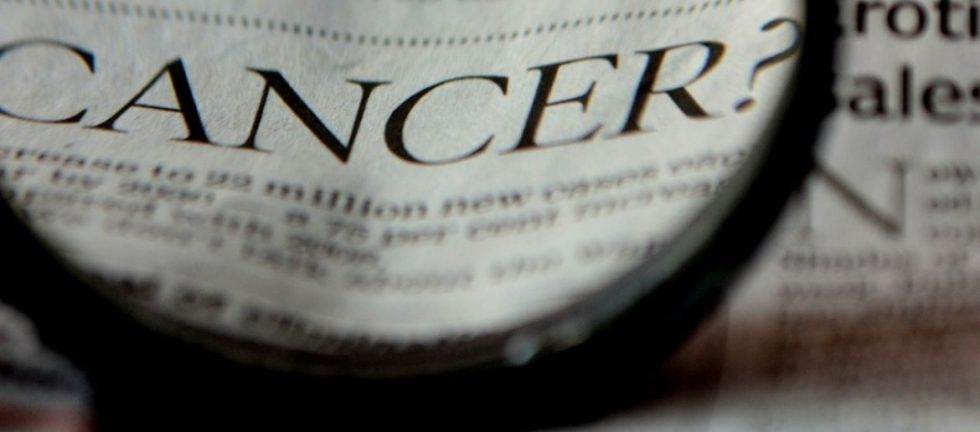 Close-up view of a magnifying glass over a newspaper headline reading "CANCER?".