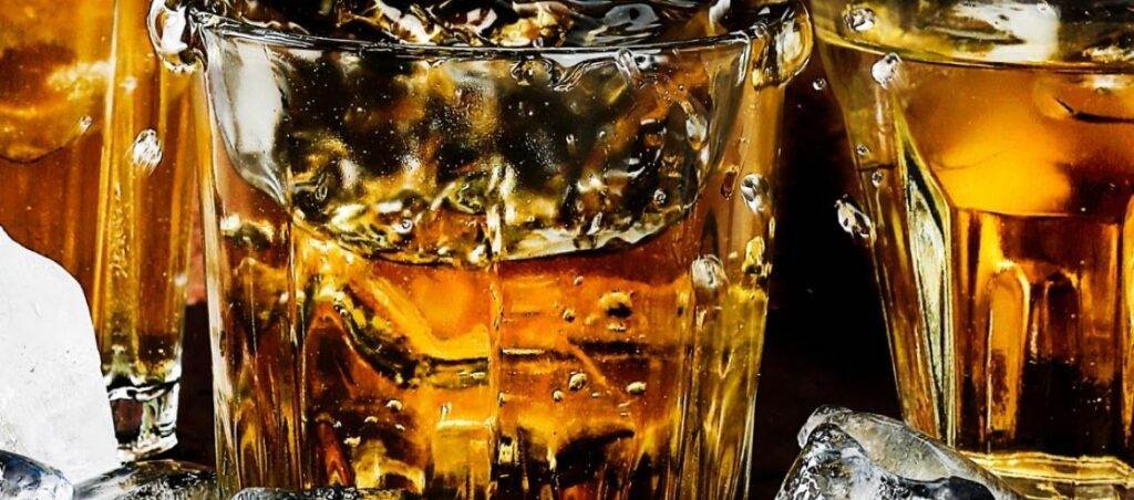 Three glasses of amber liquid, ice cubes, close-up. Drink driving consequences.