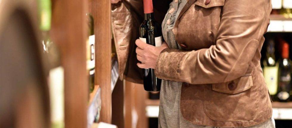 Woman selecting a bottle of red wine from a store shelf.
