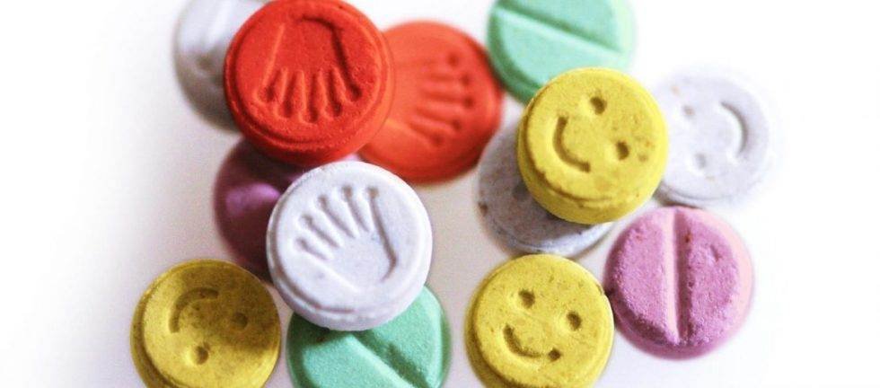 Colorful ecstasy pills with various designs, including smiley faces and a crown. Pill testing at festivals.
