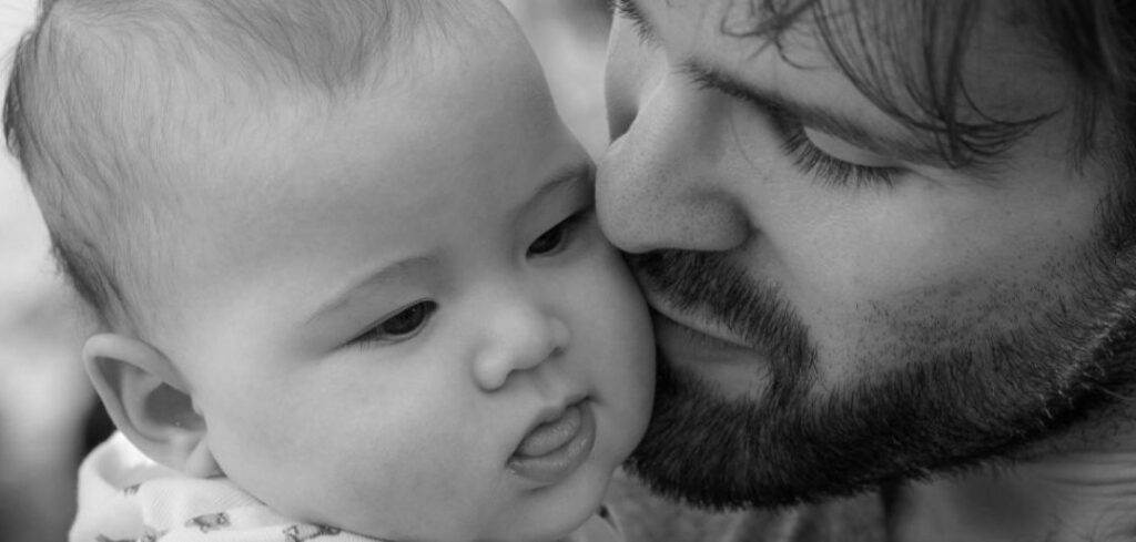 Close-up of a father tenderly kissing his baby's cheek.