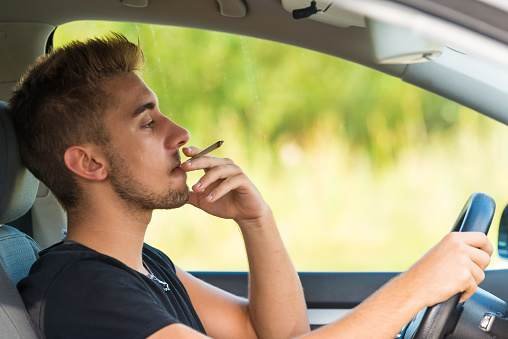 Man driving car and smoking a joint. NSW drug driving penalties.