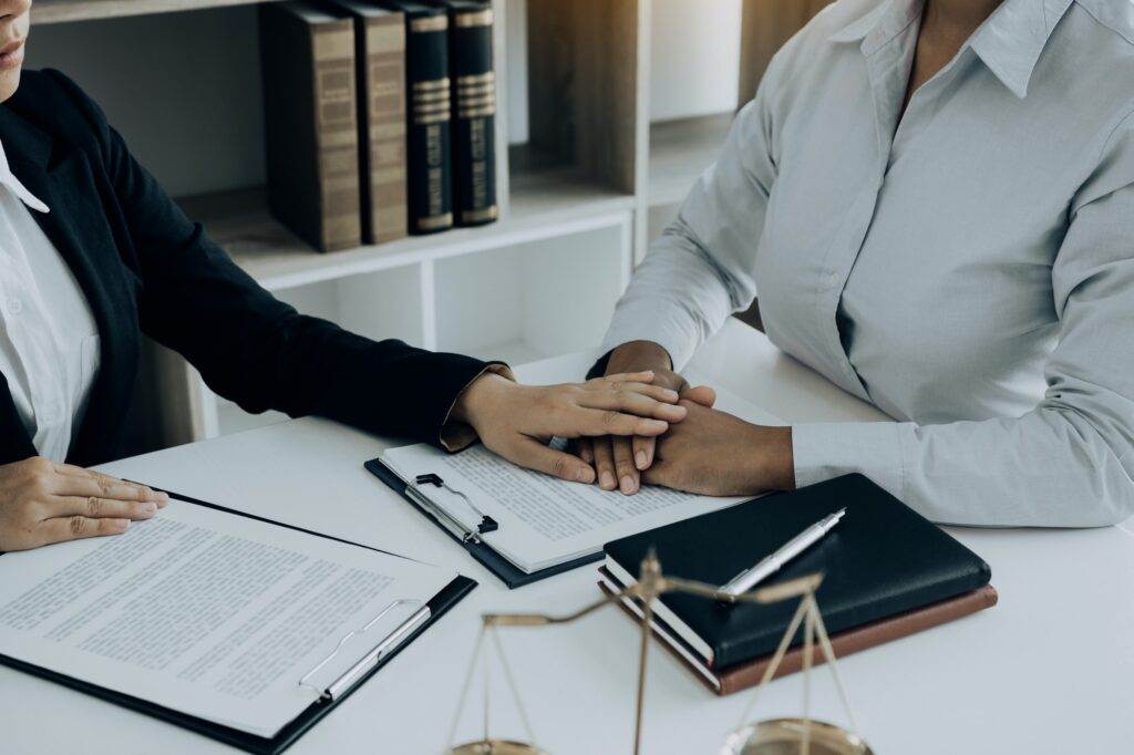 Lawyer and client shaking hands, legal documents on table.
