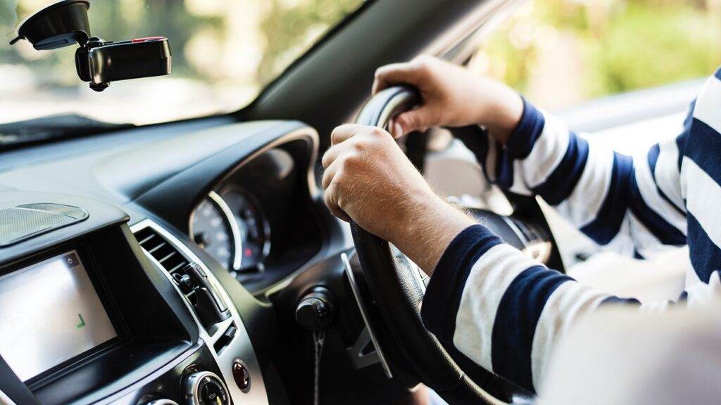 Person's hands gripping a car's steering wheel while driving. Driving with an expired license is illegal.