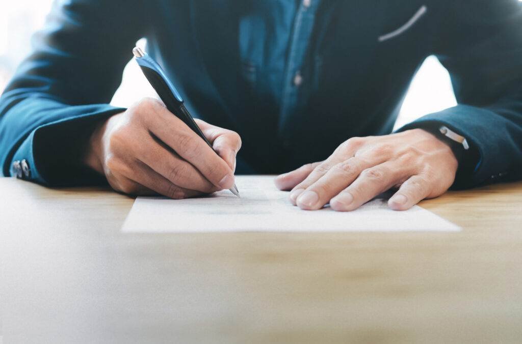 Person signing a legal document, writing an apology letter to the court for driving offences.