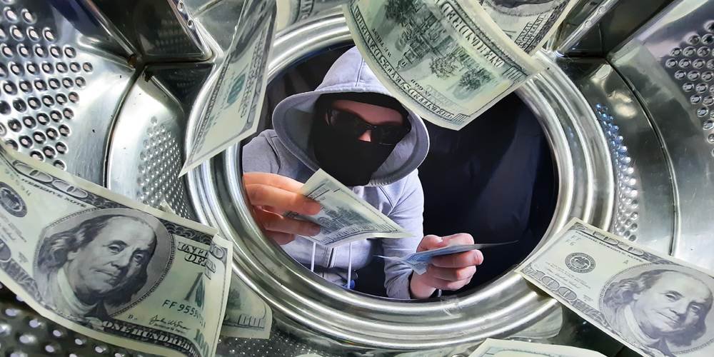 Person in hoodie hiding money inside a washing machine, illustrating money laundering.