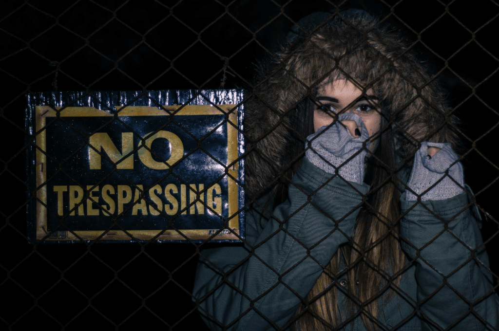 Person in winter clothing behind fence with "No Trespassing" sign, illustrating difference between trespass and breaking and entering NSW.