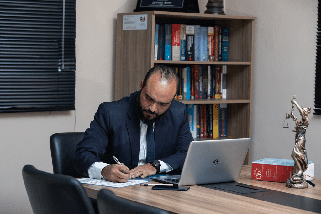 Man in a suit writing at desk with legal books and scale statue, illustrating duress defence explained in law.