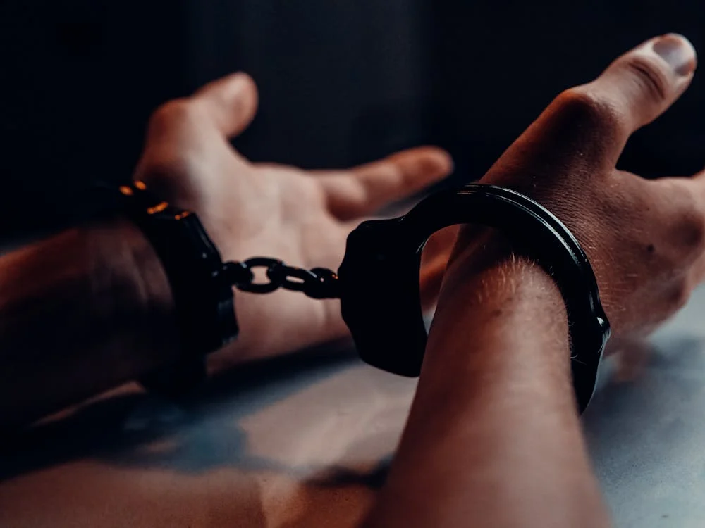 Hands in handcuffs on a table, representing Receiving Stolen Goods in NSW: Understanding Offence and Defence in Criminal Law.