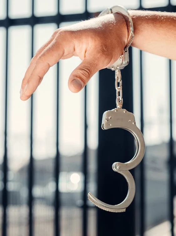 Handcuffed hand in focus with jail bars in the background, illustrating legal context for NSW MERIT Program guide.