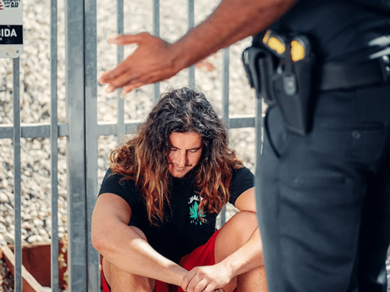 Person seated on the ground by a fence with a police officer standing nearby, related to Community Correction Orders in NSW.