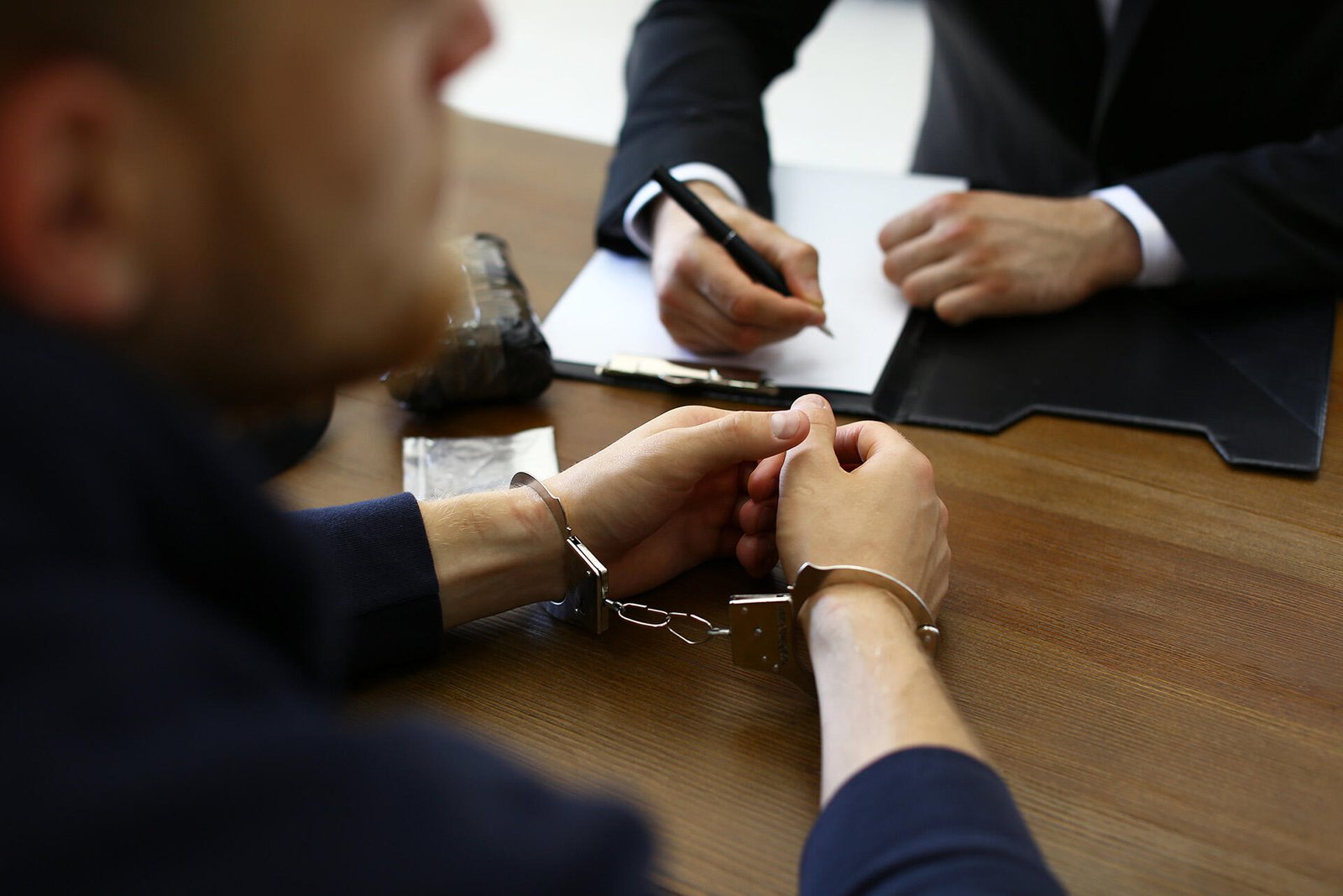 Man in handcuffs at a table with a person writing, illustrating NSW Conditional Release Orders: CRO in New South Wales.