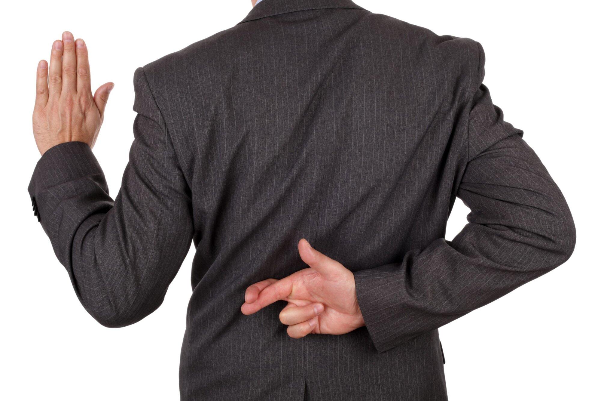 Man in suit taking oath with crossed fingers behind back, symbolizing perjury and false statements in NSW court offenses.