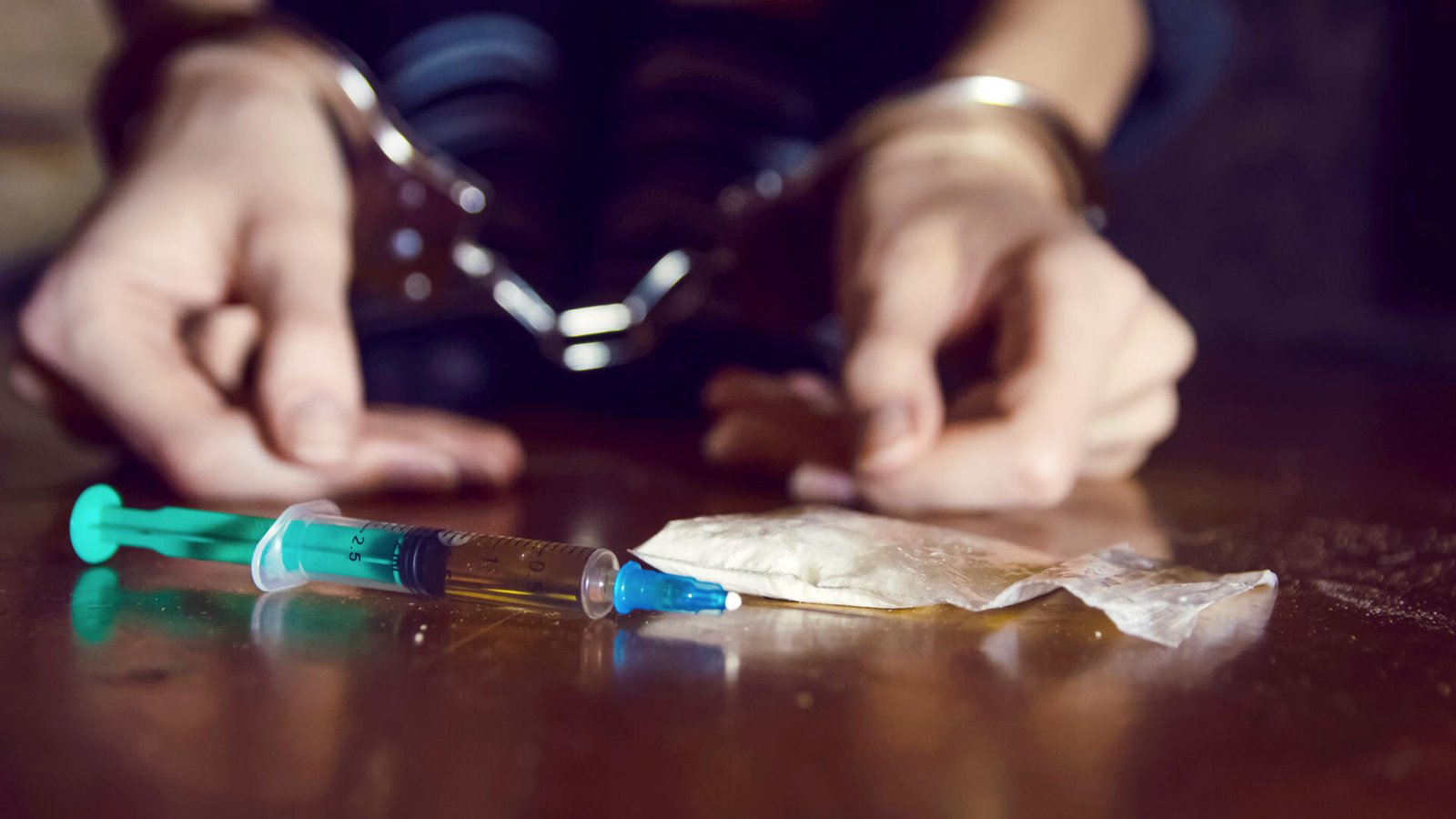 Handcuffed individual with drugs and syringe, illustrating ongoing drug supply offense and penalties in NSW.