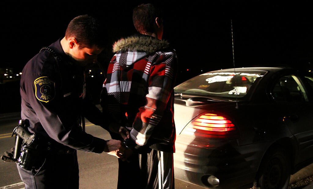 Police officer arresting person near car at night, illustrating consequences of being drunk in public.