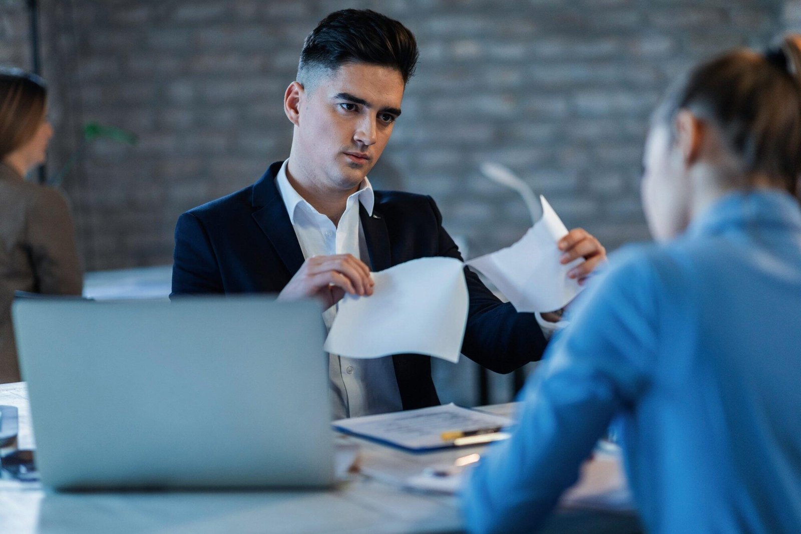 Man tearing a document in an office setting, symbolizing dishonesty offences in NSW, with a laptop in the foreground.
