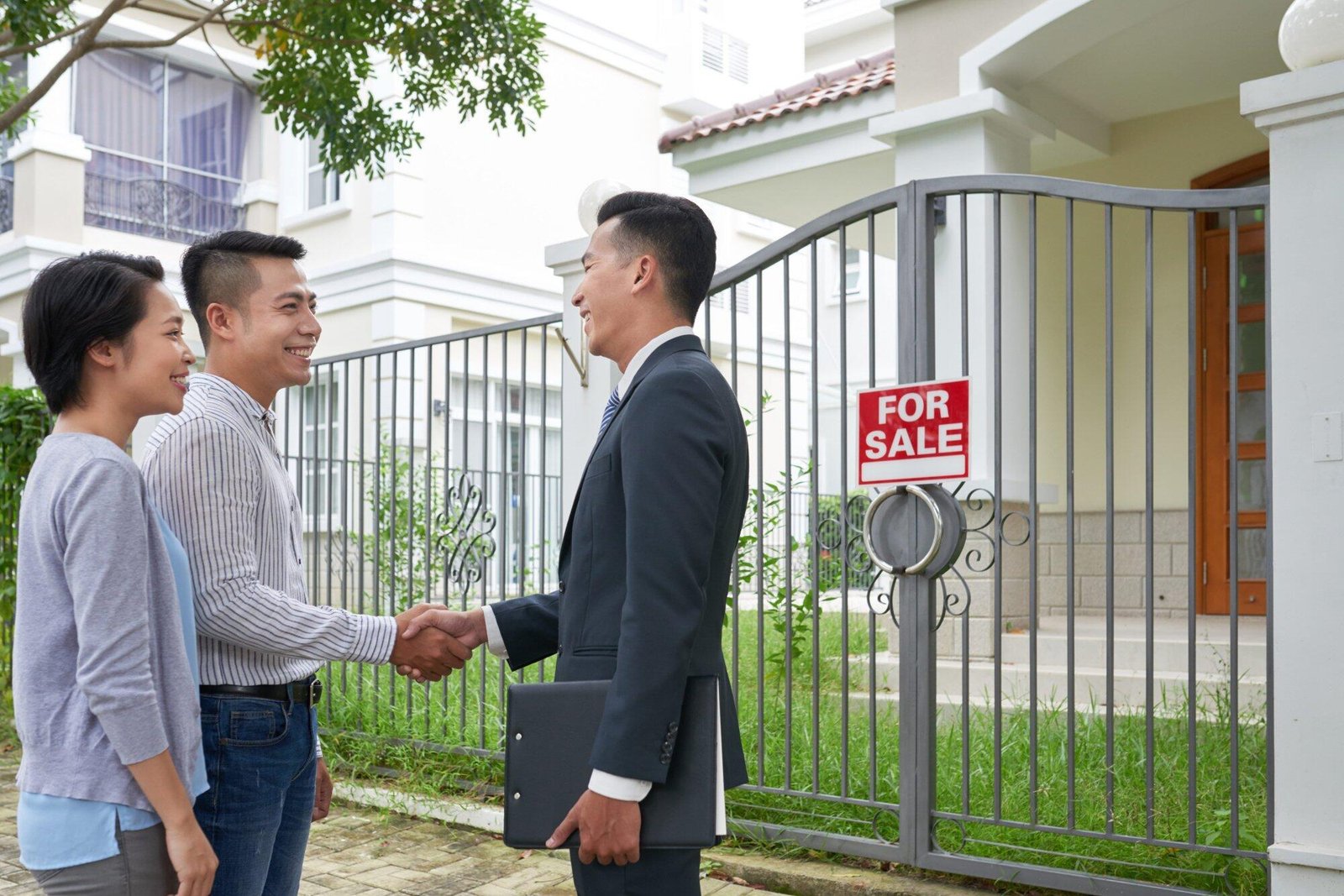 Couple shaking hands with realtor outside a house with a "For Sale" sign, relevant to property offences NSW context.