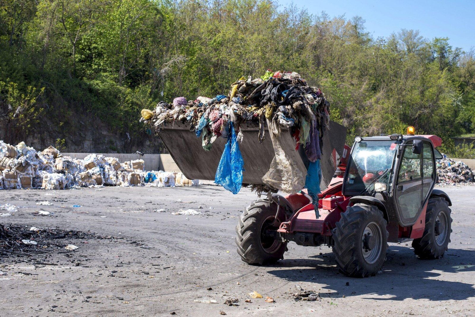 A tractor clearing a large pile of garbage in NSW, highlighting littering issues amidst a scenic forest backdrop.