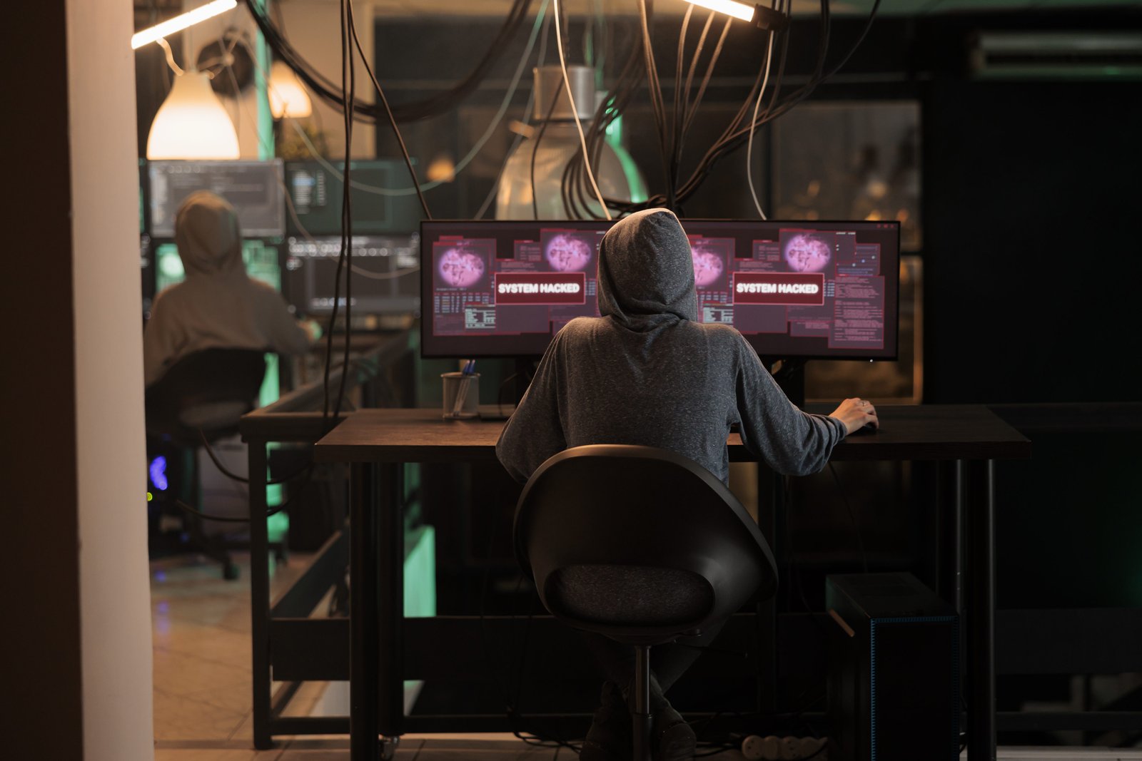 Person in hoodie at a desk with hacked system screens, representing cybercrime offences in NSW.