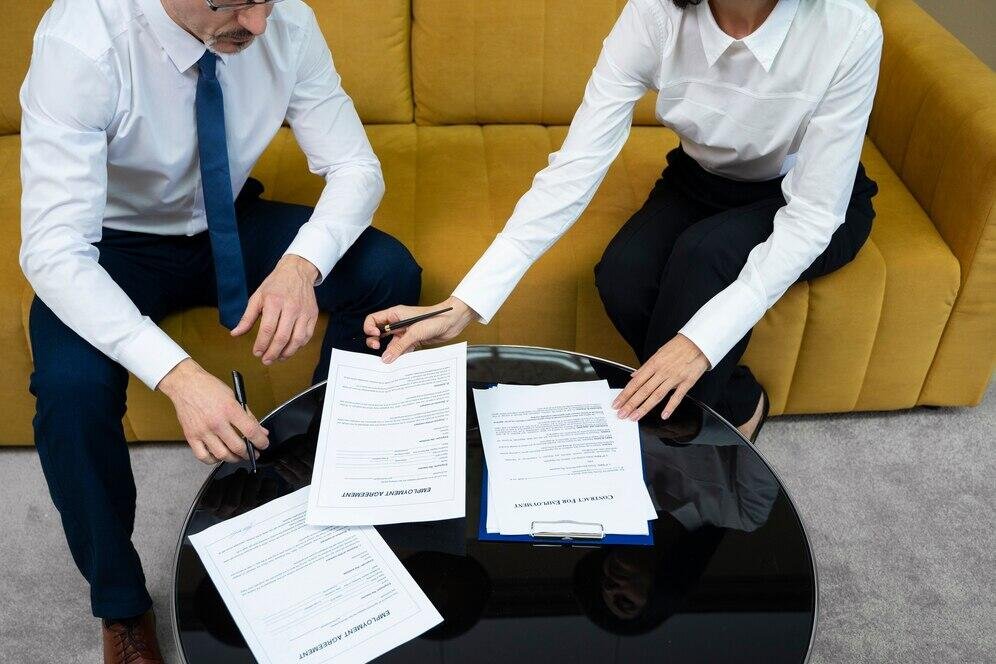 Two people review legal documents on a table, discussing potential compensation for wrongful conviction.