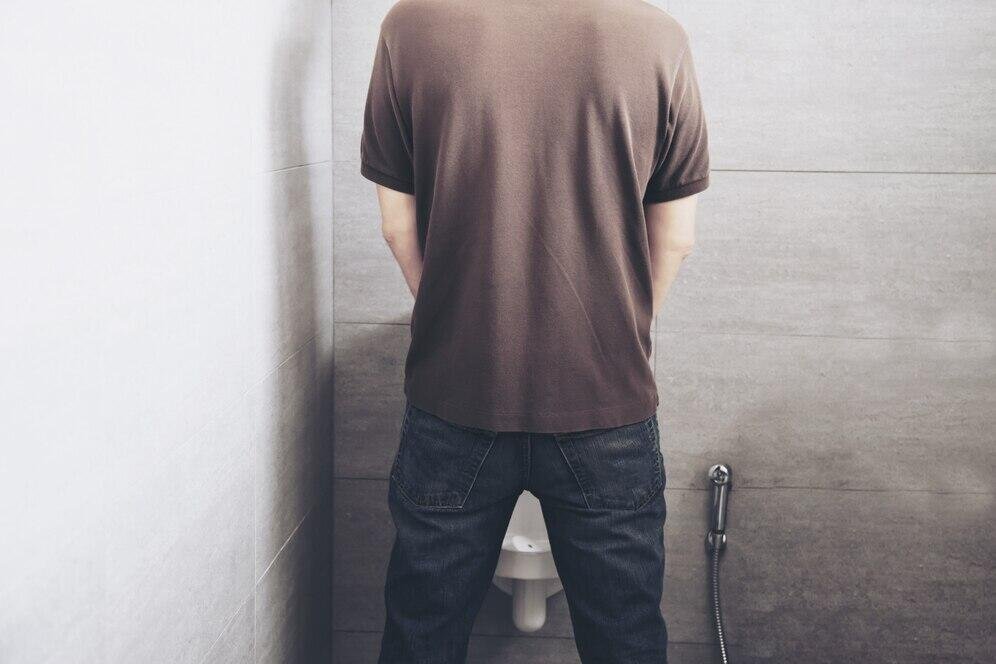 Person standing by a urinal in a public restroom. Discusses legality of peeing in public.