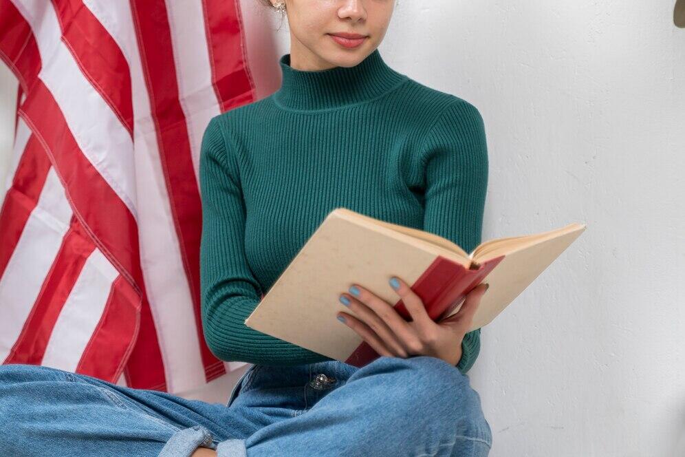 Woman reading a book near an American flag.
