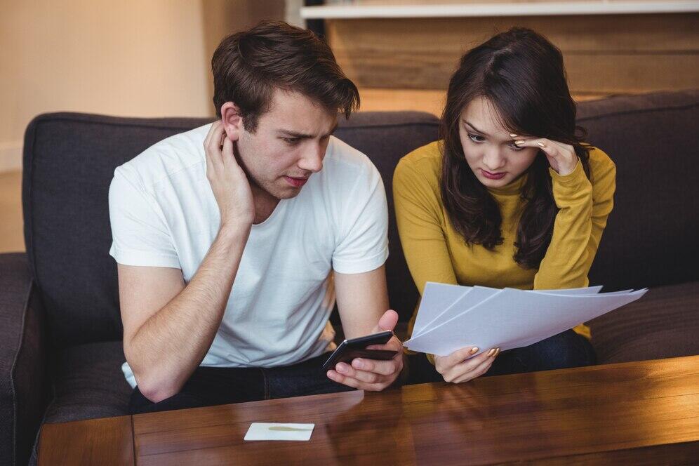 Worried couple reviewing documents at home, possibly facing financial difficulties.