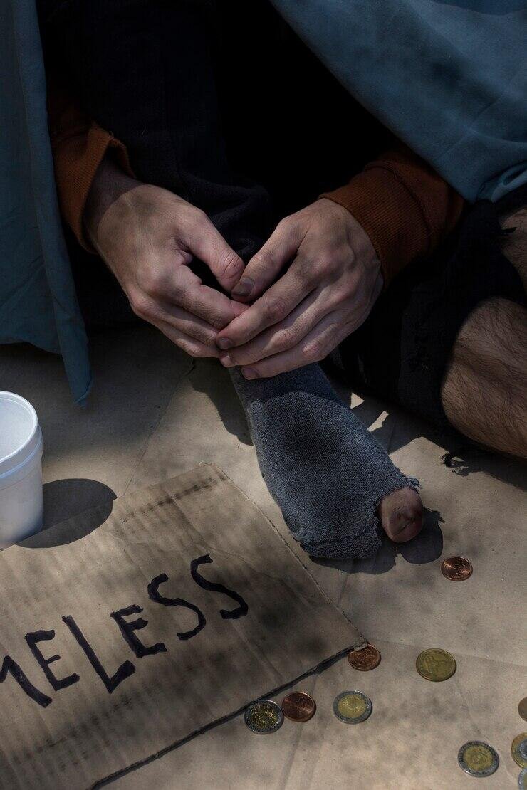 Homeless person with sign reading "Homeless" and coins on the ground.