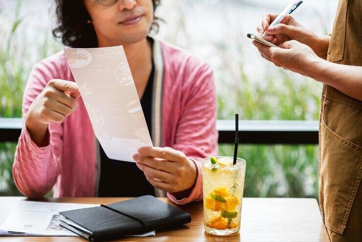 Person looking at restaurant menu, waitress taking order. NSW food safety.