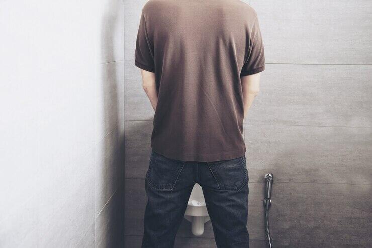 Man using a urinal in a public restroom. Public urination offences in Australia.