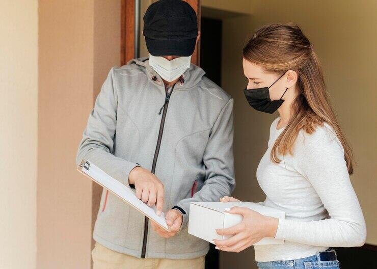 Delivery person and customer wearing face masks exchange a package.