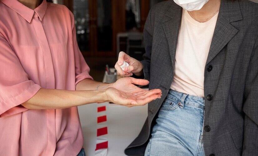 Two women applying hand sanitizer, practicing safety measures.