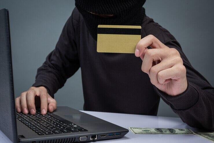 Masked person holding a credit card at a laptop, illustrating Centrelink fraud.