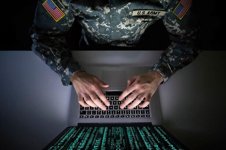 Soldier using laptop, code visible on screen. Digital piracy risk.